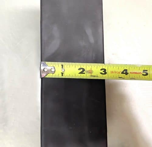 A tape measure is measuring the length of a black object.