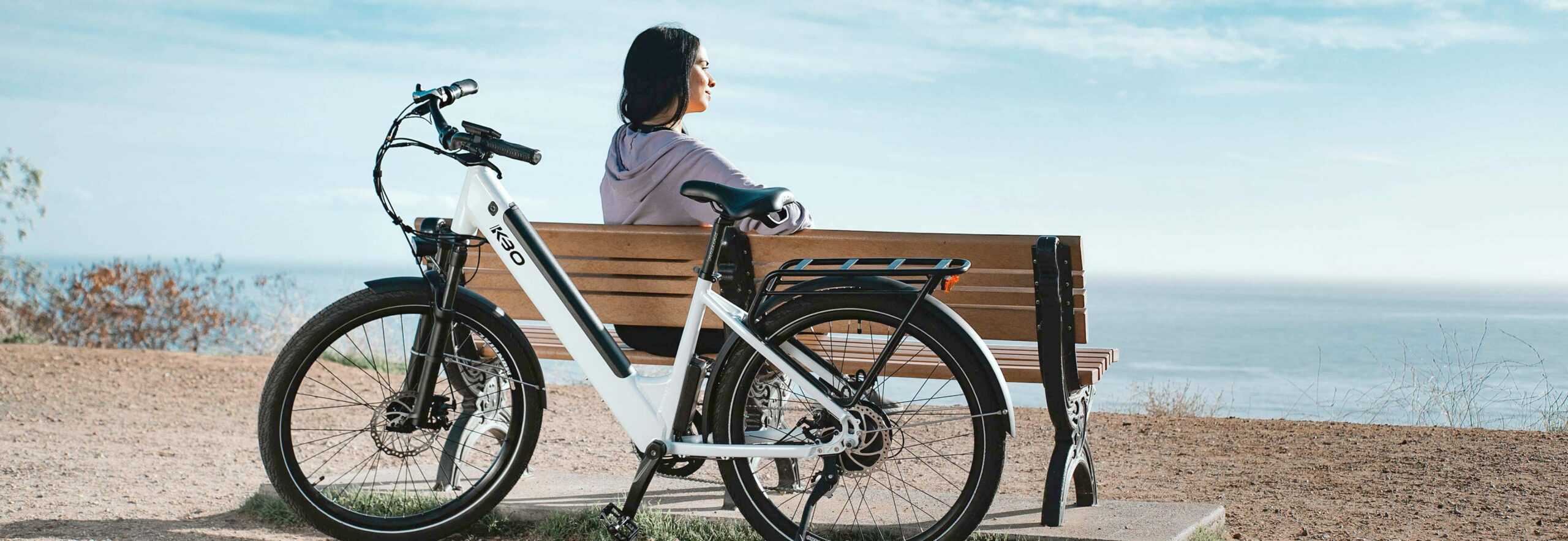 A woman sitting on top of a bench next to her bike.